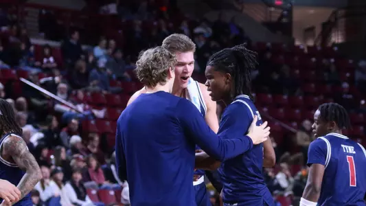 Collin Tanner is embraced by Mike Walz and Kirby Mooney coming off the court