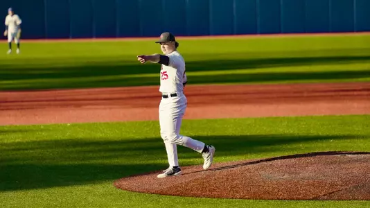 Tyler Rigot in an all white Spider Baseball uniform walks off the mound pointing at his catcher