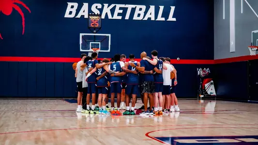 The men's basketball team huddles at midcourt during a practice