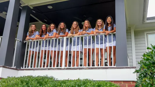 The women's golf team stands on a porch at Independence Golf Club