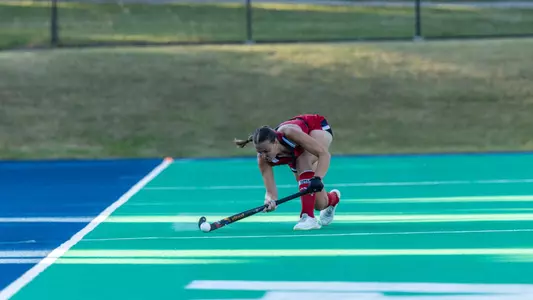 Spider field hockey defender Madelyn Curtis wearing all red uniform sends the ball up the field