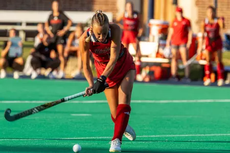 Lainey Nichols, wearing all red Spider field hockey uniform, swings her stick at the ball