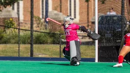 Spider field hockey goalkeeper Thea Conomikes in an all pink uniform makes a kick save