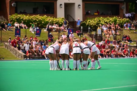 Spider field hockey in their all-white uniforms with red numbers huddles prior to the start of the game.
