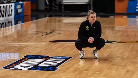 Alisa Kresge kneels next to a March Madness sign