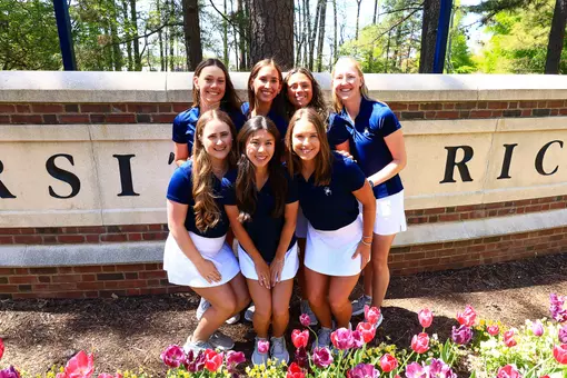 Women's golf team poses in front of a sign on campus