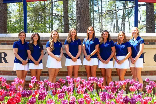 The women's golf team poses in front of the concrete University of Richmond sign