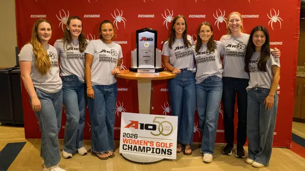 The women's golf team poses in front of a red backdrop