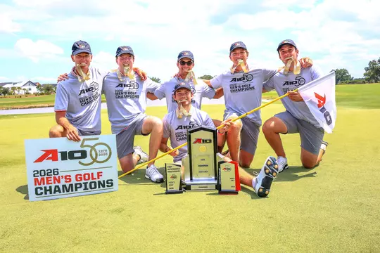 The men's golf team bites their gold medals while kneeling on the 18th green at Evermore Resort.