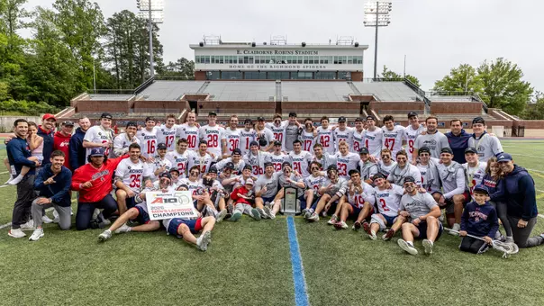 Richmond men's lacrosse team huddles around the 2026 Atlantic 10 Men's Lacrosse Championship trphiy