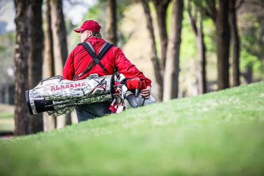 Canon Claycomb looking over his shoulder carrying an Alabama golf bag