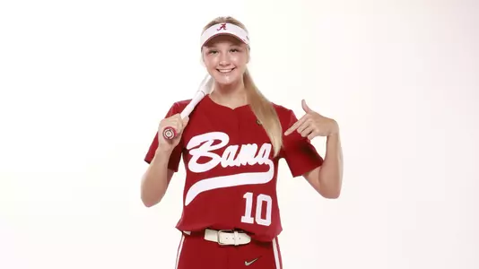 Alabama softball player Abby Duscherer poses with bat and points at her jersey.