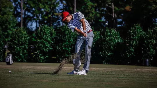 Dirt flying into the air as Jack Goldasich hits the golf ball