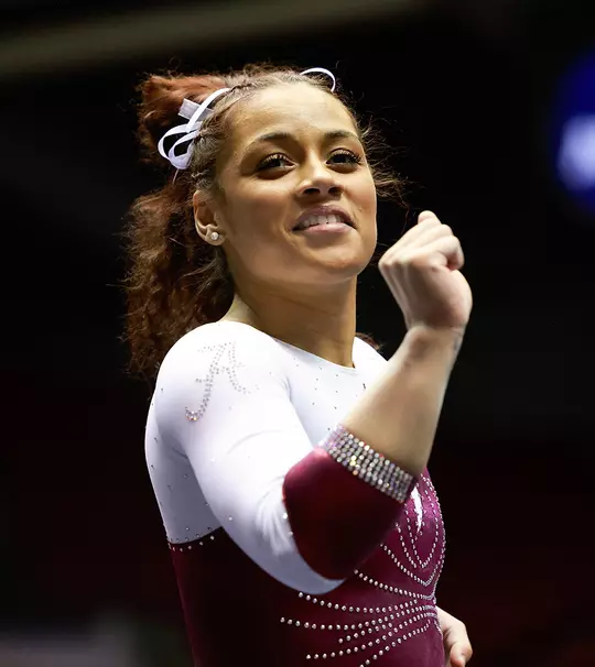 Makarri Doggette in a leotard with her fist raised in the air and a smile on her face