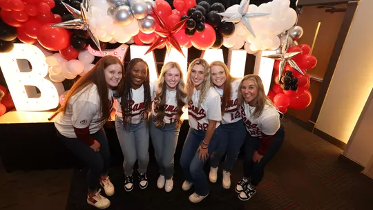 Softball players posing in front of arranged balloons