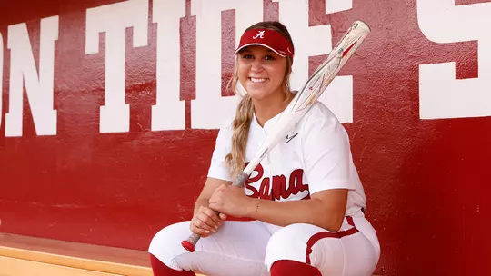 Ashley Prange sitting on the bench in the dugout holding a bat