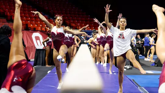 Luisa Blanco and other gymnasts warming up on either side of the balance beam