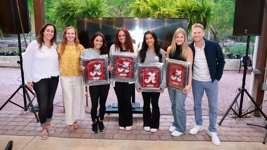 Luisa Blanco posing with her teammates and coaches holding plaques with the script A