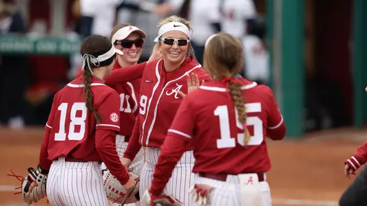 Alabama softball player Kayla Beaver smiles with her teammates on the field.