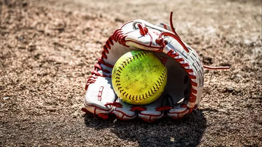 Detail photo of a softball inside a glove in the dirt