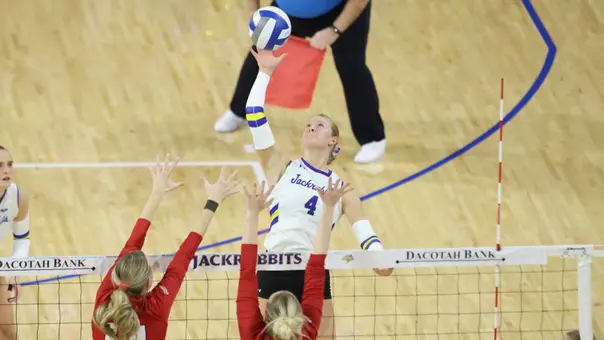 A women's volleyball player attacks a ball at the volleyball net against two defenders