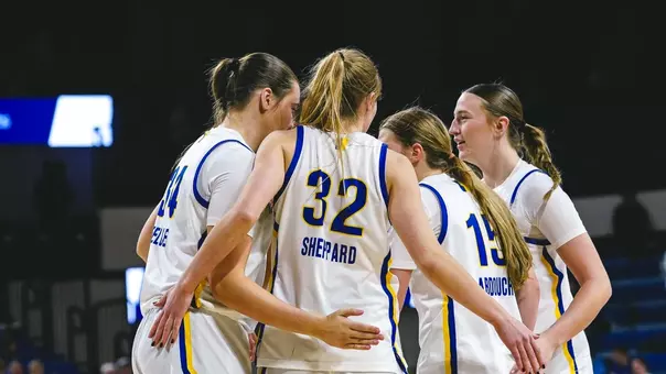 A women's basketball team in white uniforms huddles up during a game