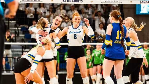 Volleyball players in white and blue uniforms celebrate during a match at First Bank & Trust Arena