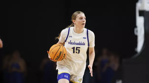A women's basketball player in a white uniform dribbles a basketball during a game