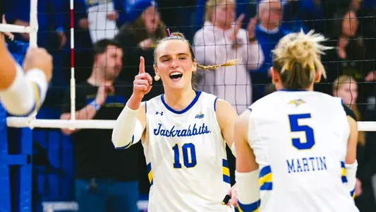 A women's volleyball player in a white jersey celebrates a point during a volleyball match