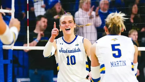 A women's volleyball player in a white jersey celebrates a point during a volleyball match