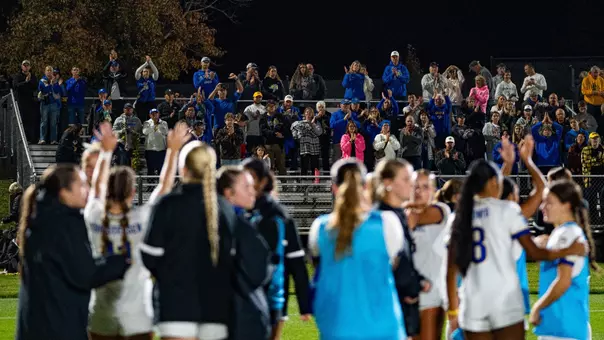 Soccer players clap on the field as fans in the stands cheer for them