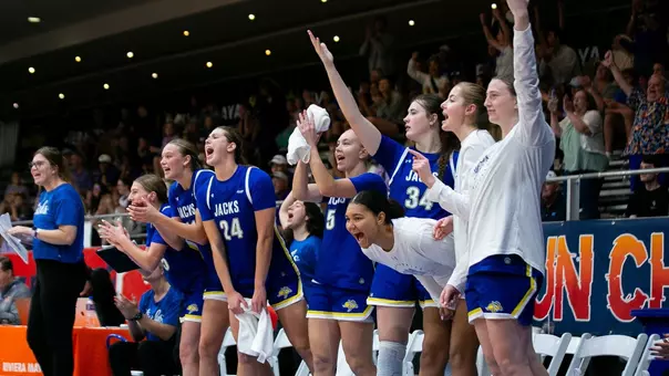 Ten members of a women's basketball team wearing blue uniforms on the bench celebrates a 3-pointer during a game