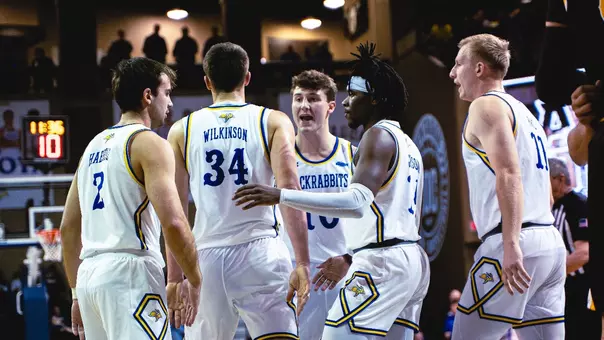 Five men's basketball players huddle up following a play