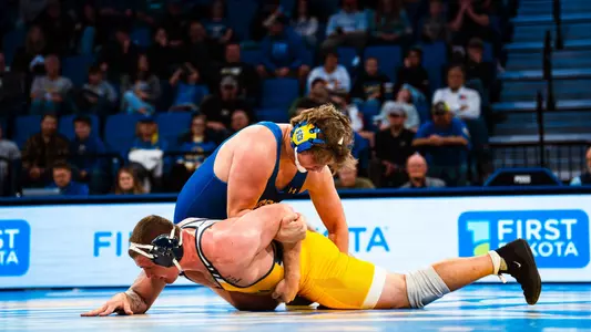 A man, Luke Rasmussen, pins the arm of another man behind his back in a wrestling match.