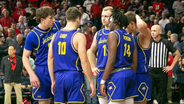 Basketball players in blue and yellow uniforms huddle on the court during a game