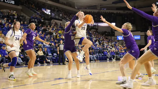 A women's basketball player, Abby Hoselton, in a white uniform goes up for a layup as players in purple uniforms defend.