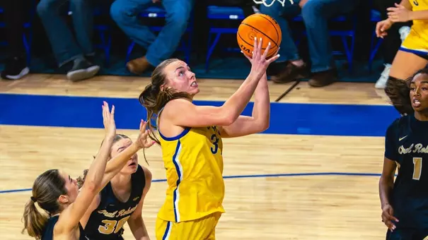 A women's basketball player in a yellow uniform, Brooklyn Meyer, shoots toward the basket as players in navy blue uniforms defend.