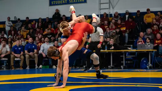 Cael Swensen, a wrestler in a blue singlet, picks up his opponent in a red singlet during a match.