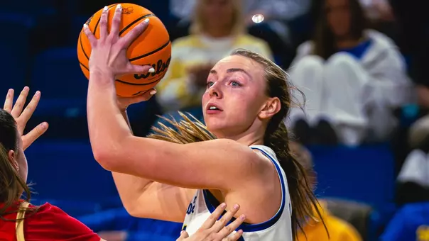 A women's basketball player, Brooklyn Meyer, holds the ball above her head and looks to pass over a defender.