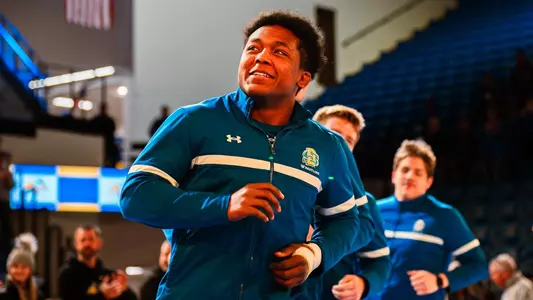 A wrestler in a blue warm-up runs out during pre-game intros.