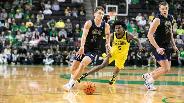 a men's basketball player in a black uniform dribbles past a defender in a yellow uniform