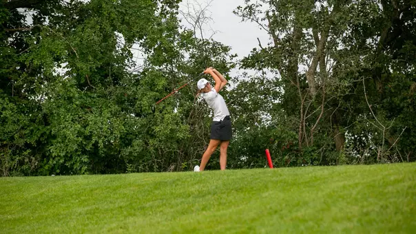 A golfer in a white polo and hat swings a golf club.