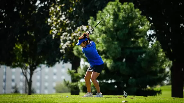A golfer in a blue polo and visor hits a golf ball with a club.