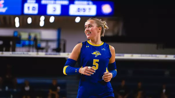 A volleyball player in a blue uniform smiles and runs during a match.