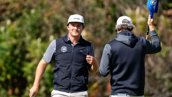 A men's golfer wearing a white hat and black vest walks off the green following a finished hole during competition