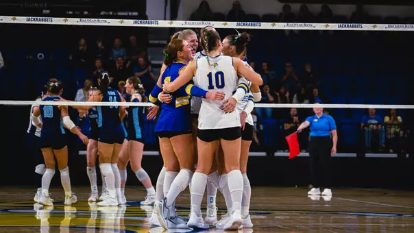 A group of volleyball players hug in a huddle after a point.