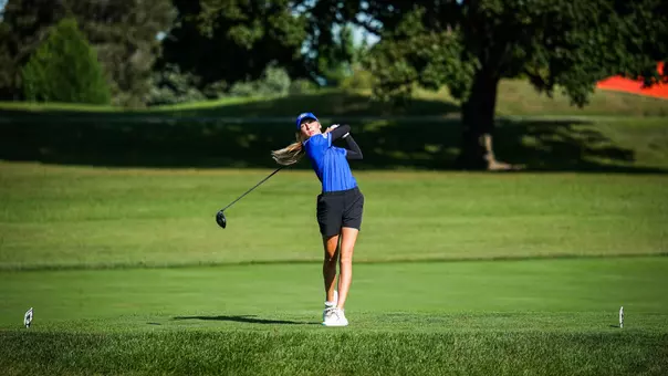 A golfer in a blue polo and cap hits a driver.