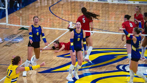 A volleyball player in a blue uniform is surrounded by players celebrating after a point.