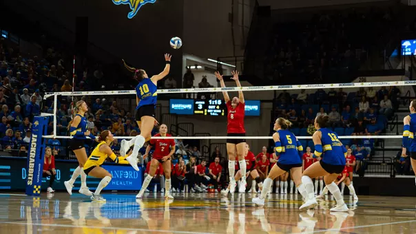 A volleyball player in blue jumps to strike a ball during a match.
