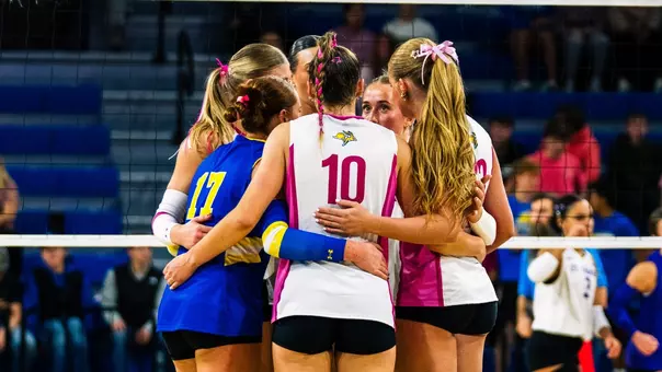 A group of players in pink jerseys huddle after a point.